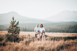 Gorgeous family of four in white in large field and mountains in the background. Happy Winsome Clients.