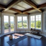 A wall of windows and timber beams overhead in a hot yoga home studio
